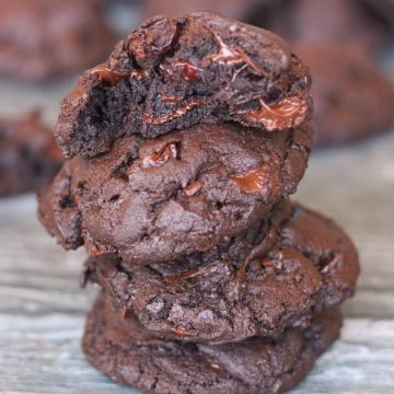Stack of four triple chocolate cherry cookies. The top cookie is broken open to reveal the gooey chocolate center.