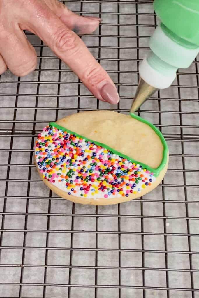 Piping green icing around the bottom half of the cookie. 