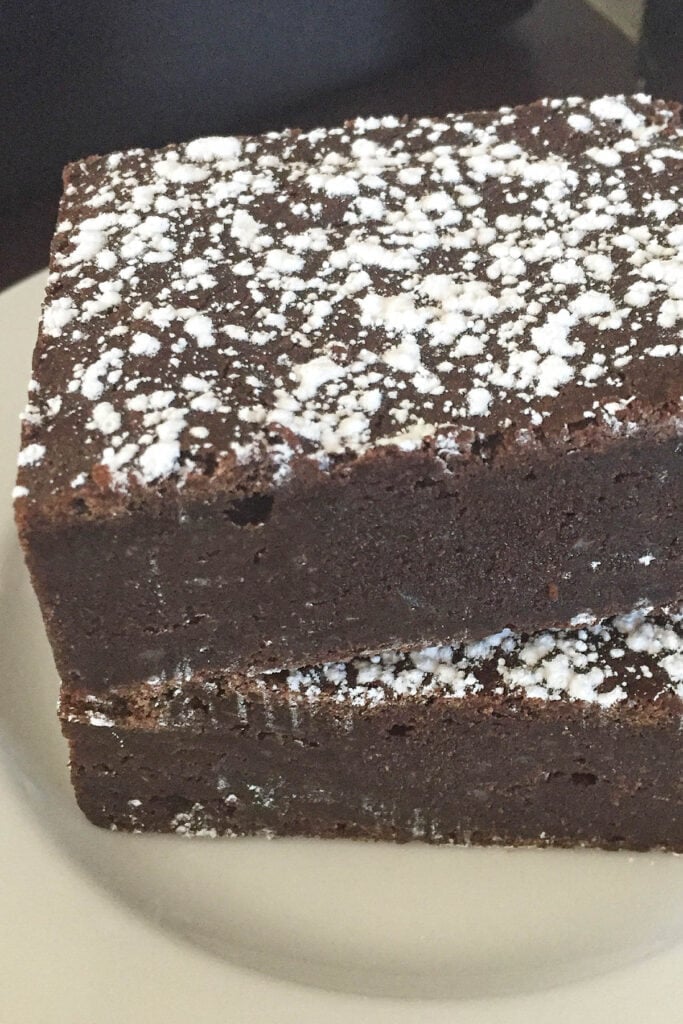 Two chocolate brownies, stacked on a plate.
