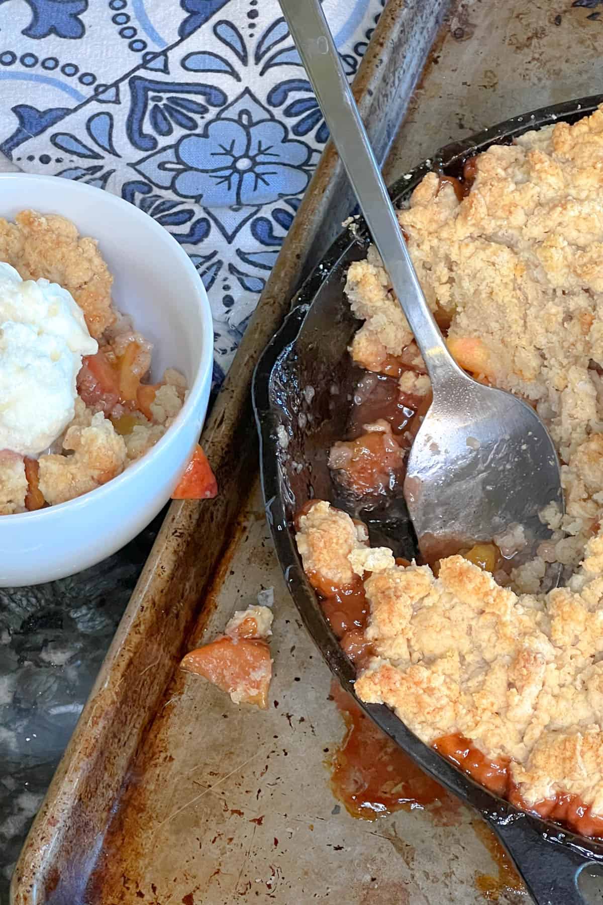 Baked skillet peach cobbler in a skillet next to a dish of peach cobbler with ice cream. 