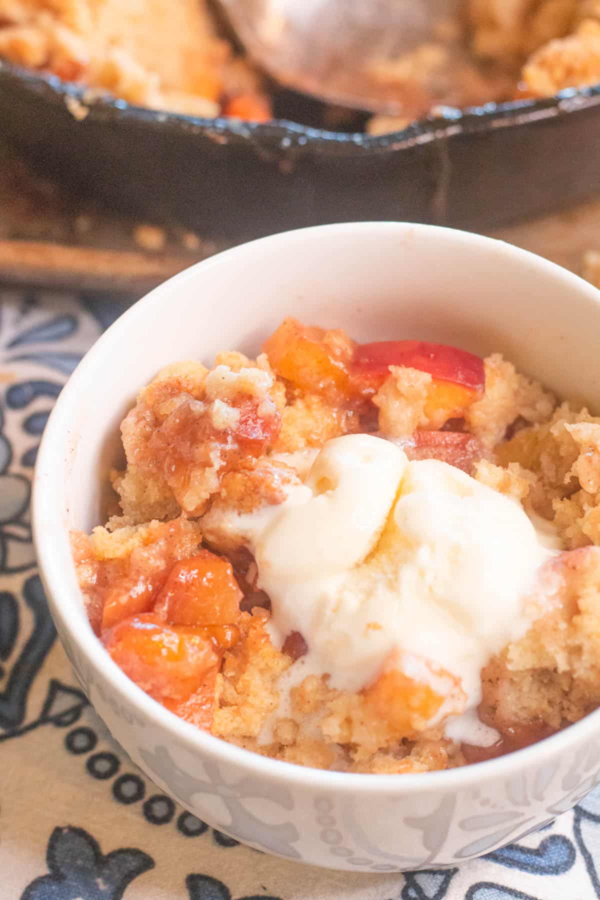 Dish of skillet peach cobbler with ice cream on top. 