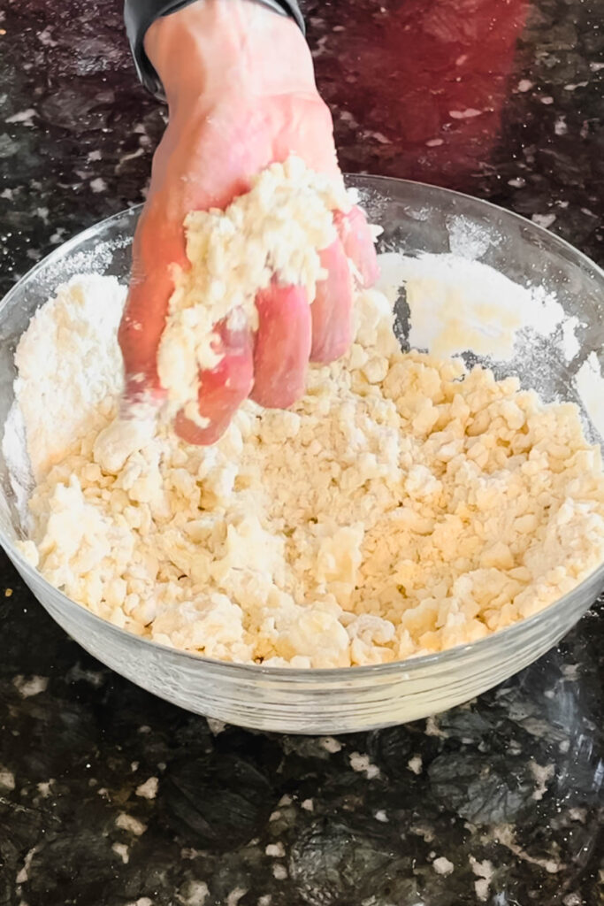 Squeezing pie crust dough mixture until it holds together shows that it is mixed properly. 