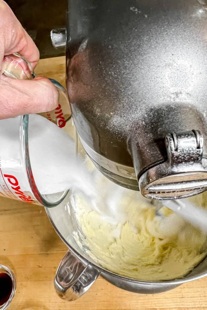 Adding sugar to the butter in a mixing bowl. 