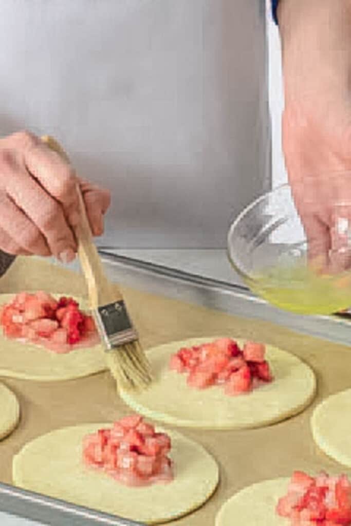 Brushing rounds of dough with egg wash.