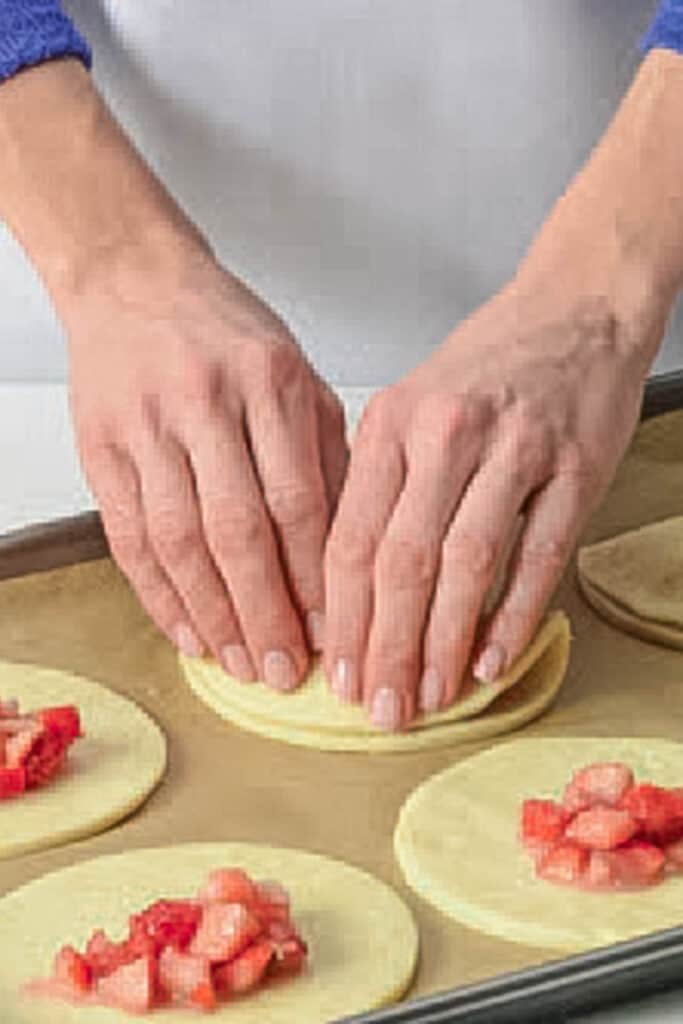 Folding over edges of dough rounds to seal. 