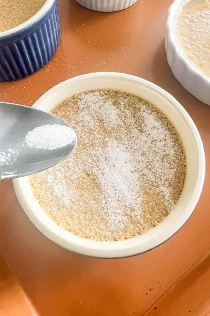 Sprinkling sugar onto the top of the chilled custards. 